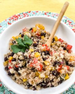 Close up of a white bowl with quinoa, black beans, and red and yellow diced bell peppers in it.