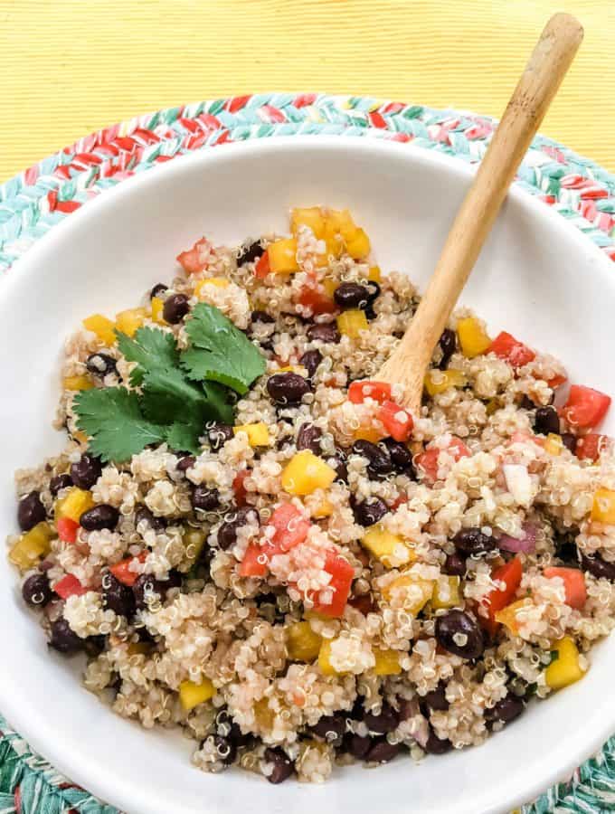 Close up of a white bowl with quinoa, black beans, and red and yellow diced bell peppers in it.
