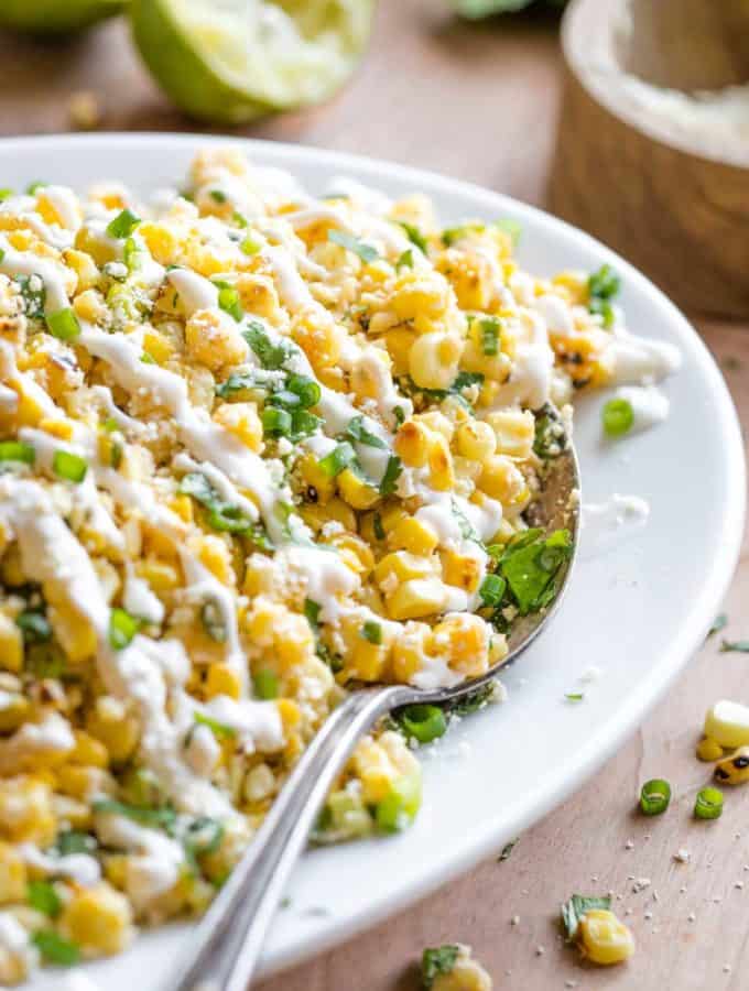 Close up of Mexican street corn salad on a white plate with a serving spoon in it.