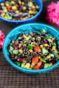 Close up of a wild rice salad with cucumber, beans, and diced tomato in a bright blue bowl.