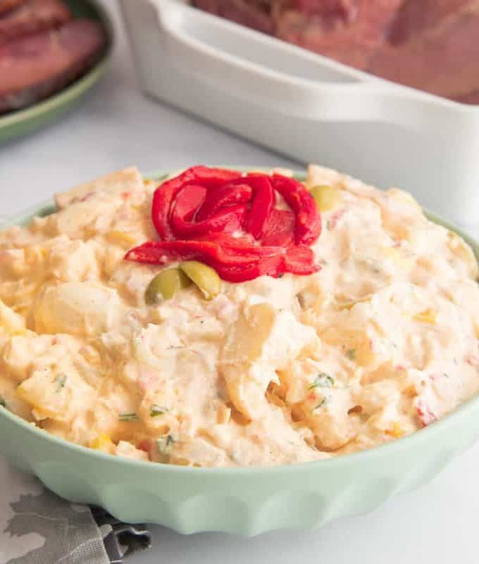 Close up of a Puerto Rican potato salad with cooked and sliced red bell peppers on the top in a light green bowl.