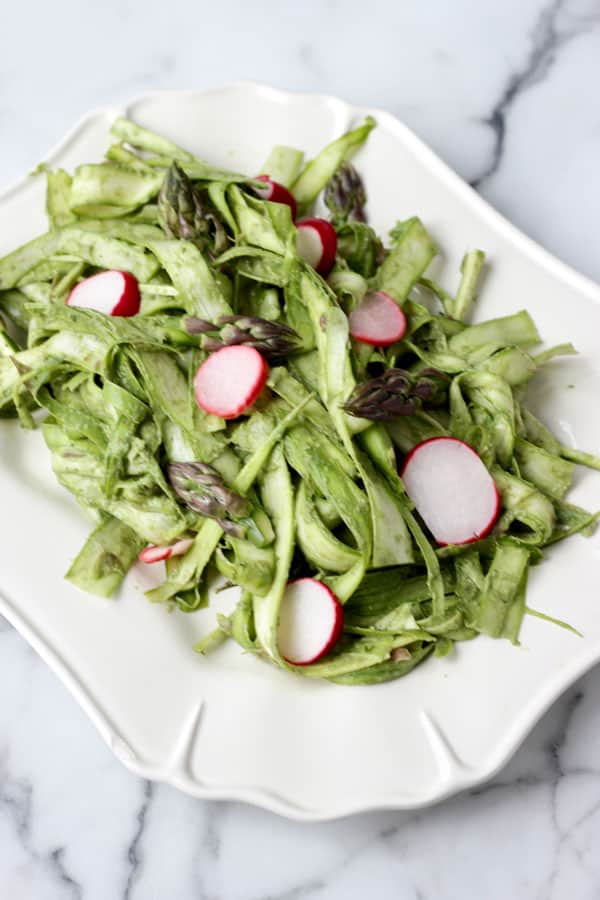 Shaved asparagus with slices of radishes on a white plate.