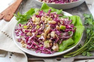 Close up of a white bean and purple cabbage salad on top of lettuce leaves on a white plate.