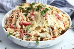 Close up of a slaw with cajun seasonings in a white bowl with fresh chopped herbs on top.