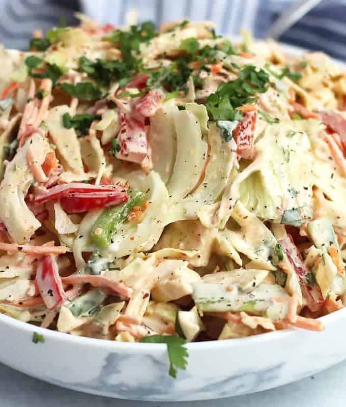 Close up of a slaw with cajun seasonings in a white bowl with fresh chopped herbs on top.