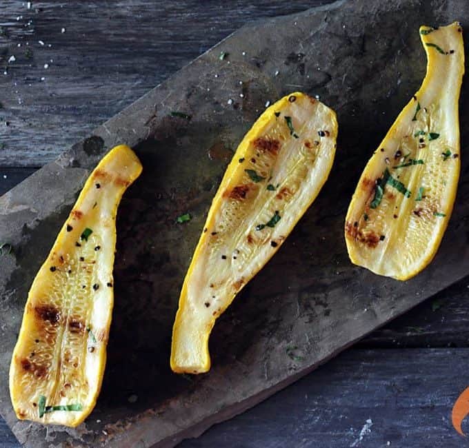 Three roasted yellow squash on a slate platter on top of a black countertop.