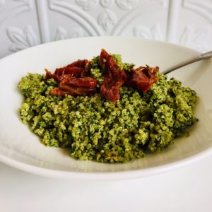 A large white bowl with some quinoa pesto salad in it, topped with sun dried tomatoes.