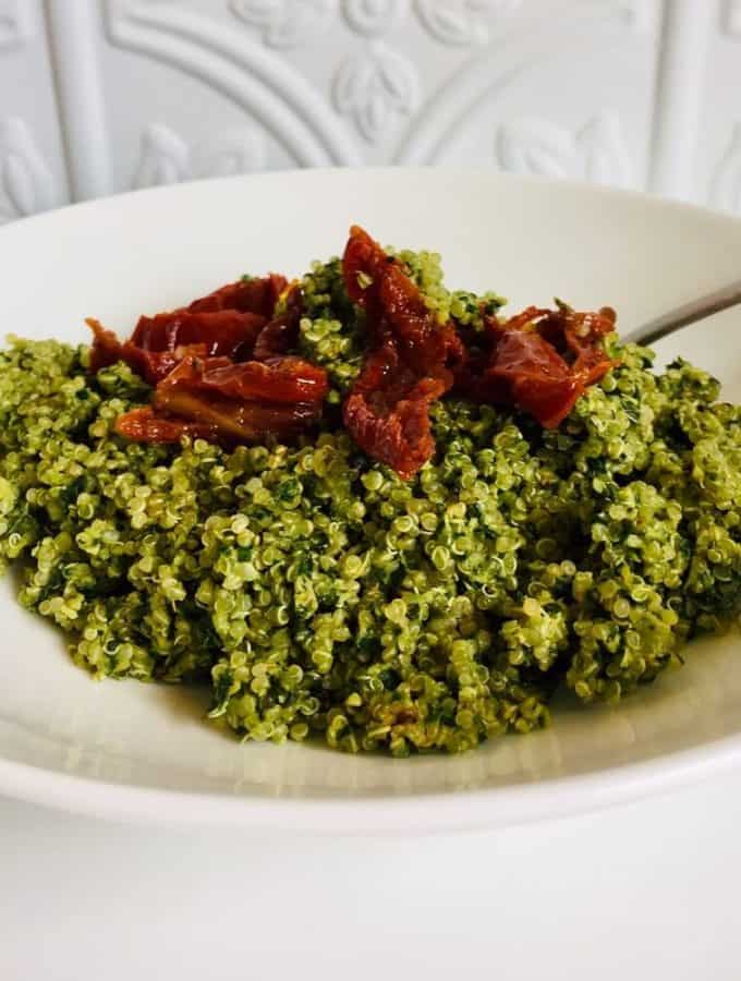 A large white bowl with some quinoa pesto salad in it, topped with sun dried tomatoes.