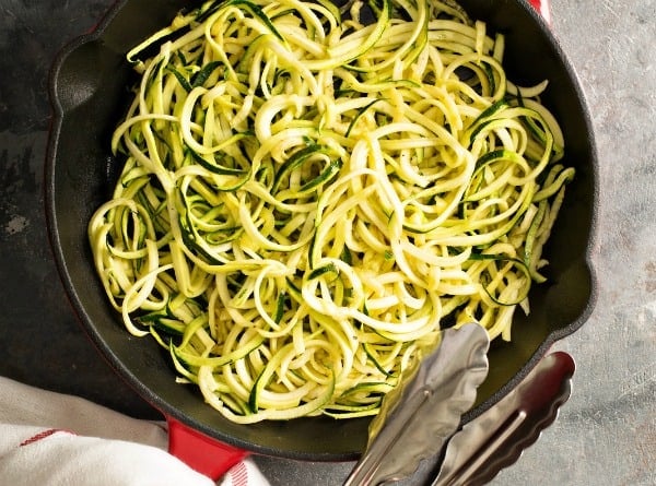 Zucchini noodles in a cast iron skillet with metal tongs to the side.