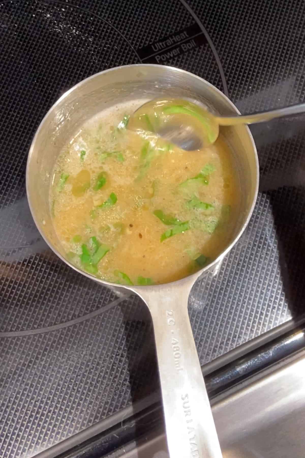 Close up of a butter herb sauce in a tiny sauce pan on the stove.