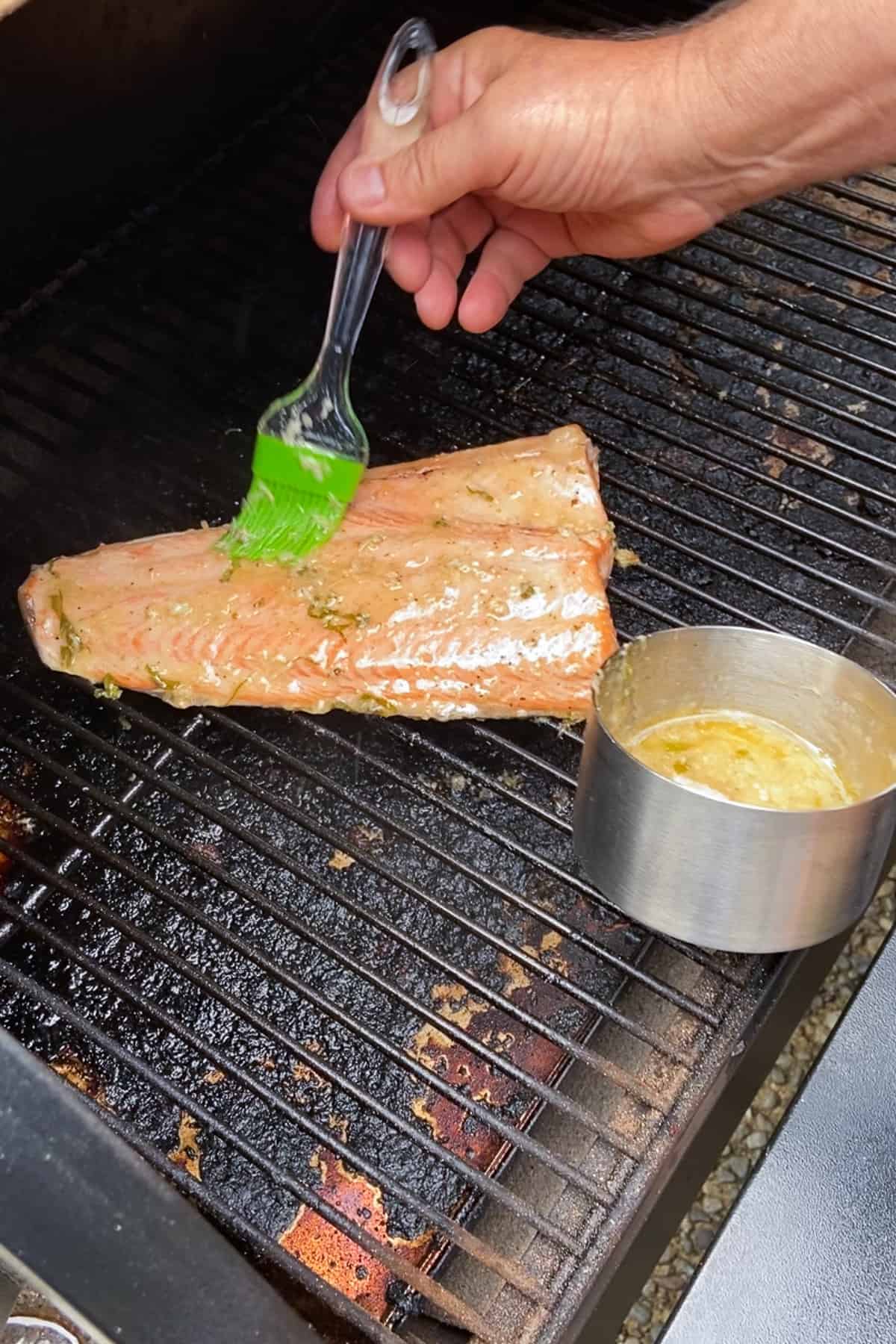 Brushing a butter sauce onto a large fillet of fish on a grill.