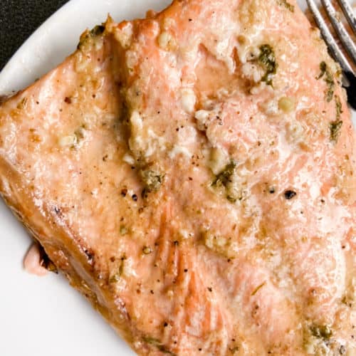 Close up of a grilled fillet of salmon on a white plate with a fork resting to the right.