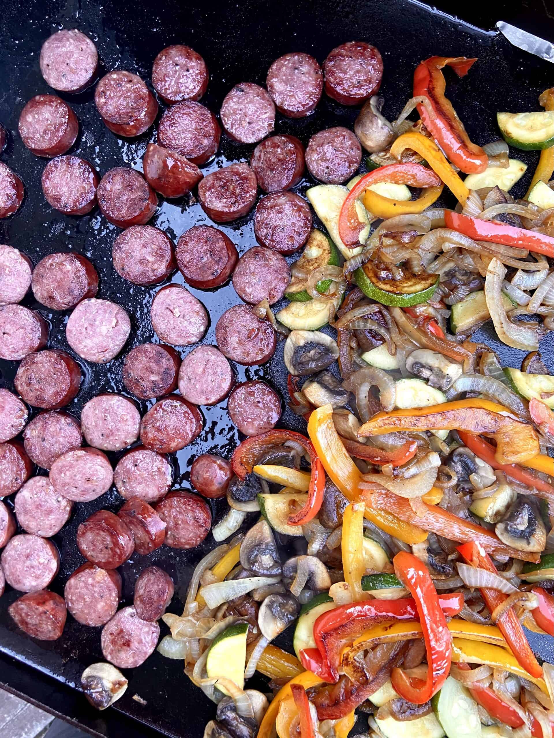 Top down shot of sliced sausage and sauteed veggies on a Blackstone griddle.