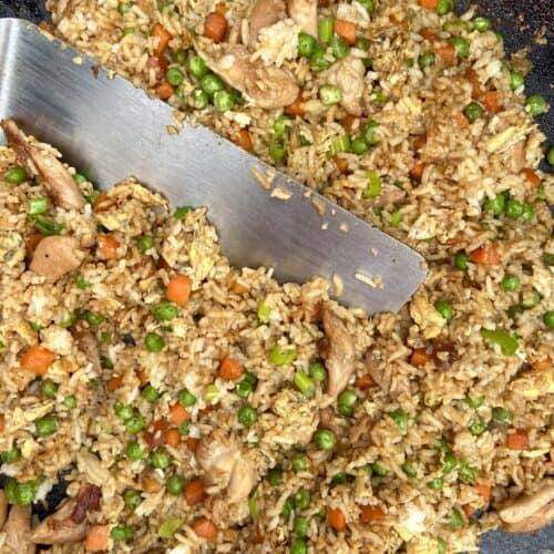 Top down shot of chicken fried rice on a Blackstone griddle with a metal spatula in it.