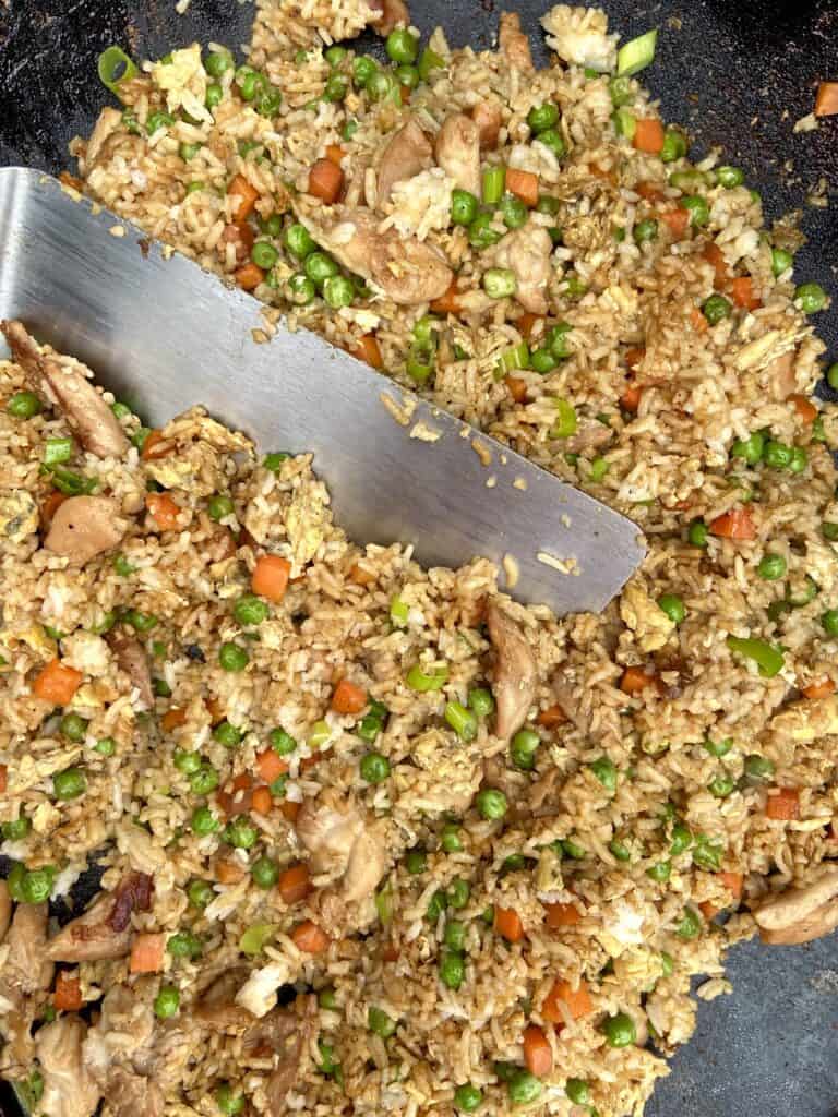 Top down shot of chicken fried rice on a Blackstone griddle with a metal spatula in it.