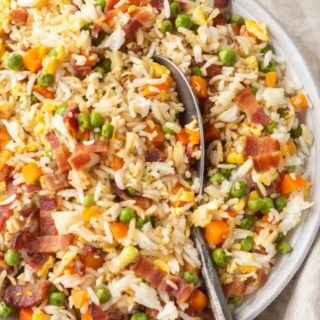 A large bowl of bacon fried rice with a large spoon in it.