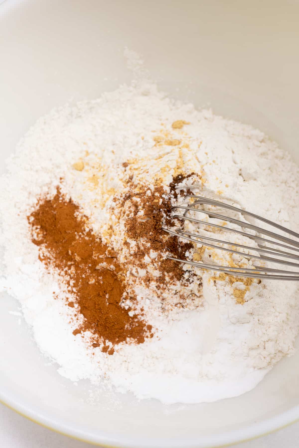 Flour and spices in a bowl with a whisk in them.