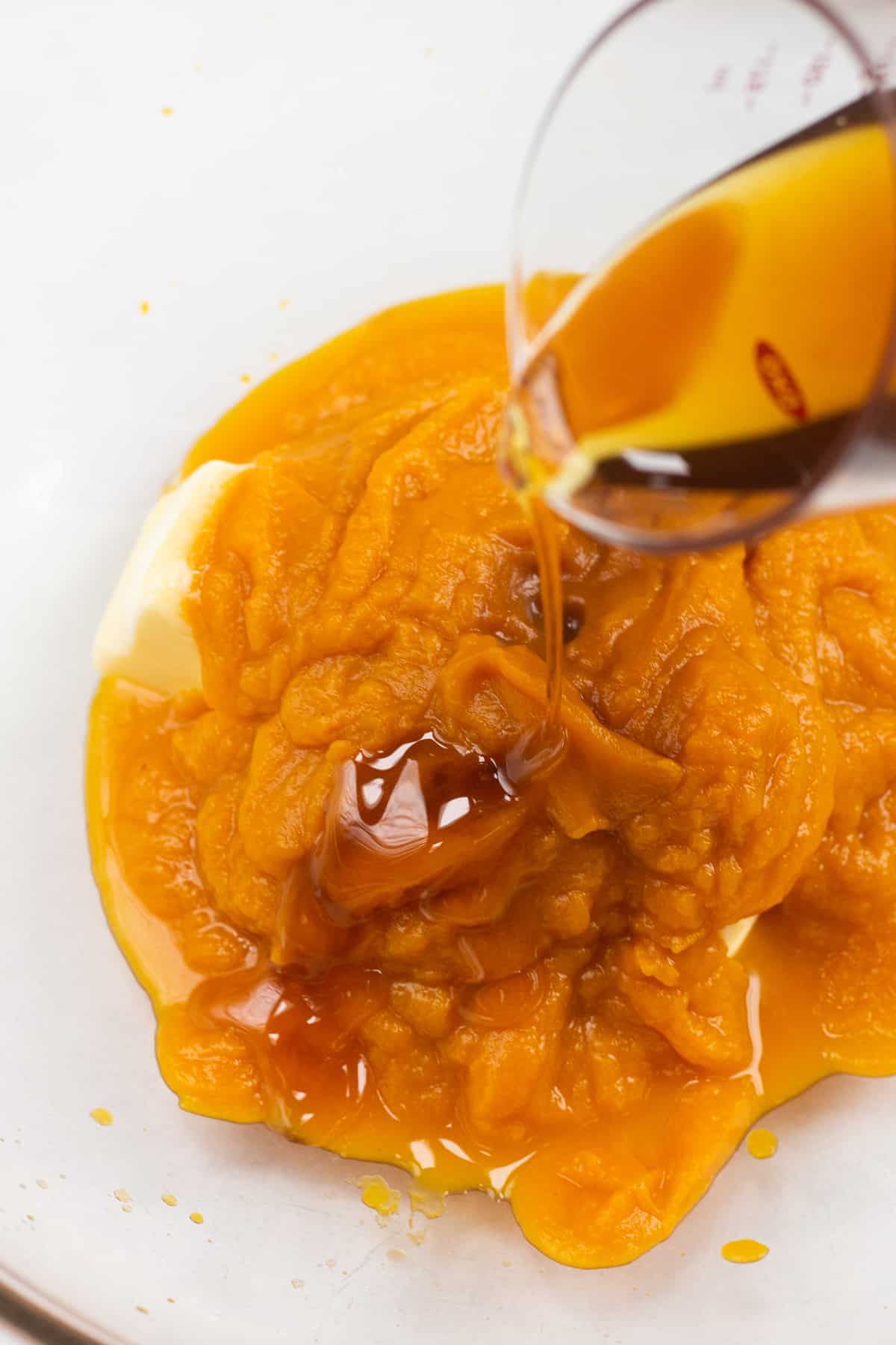 Pouring maple syrup over pumpkin puree and butter in a bowl.