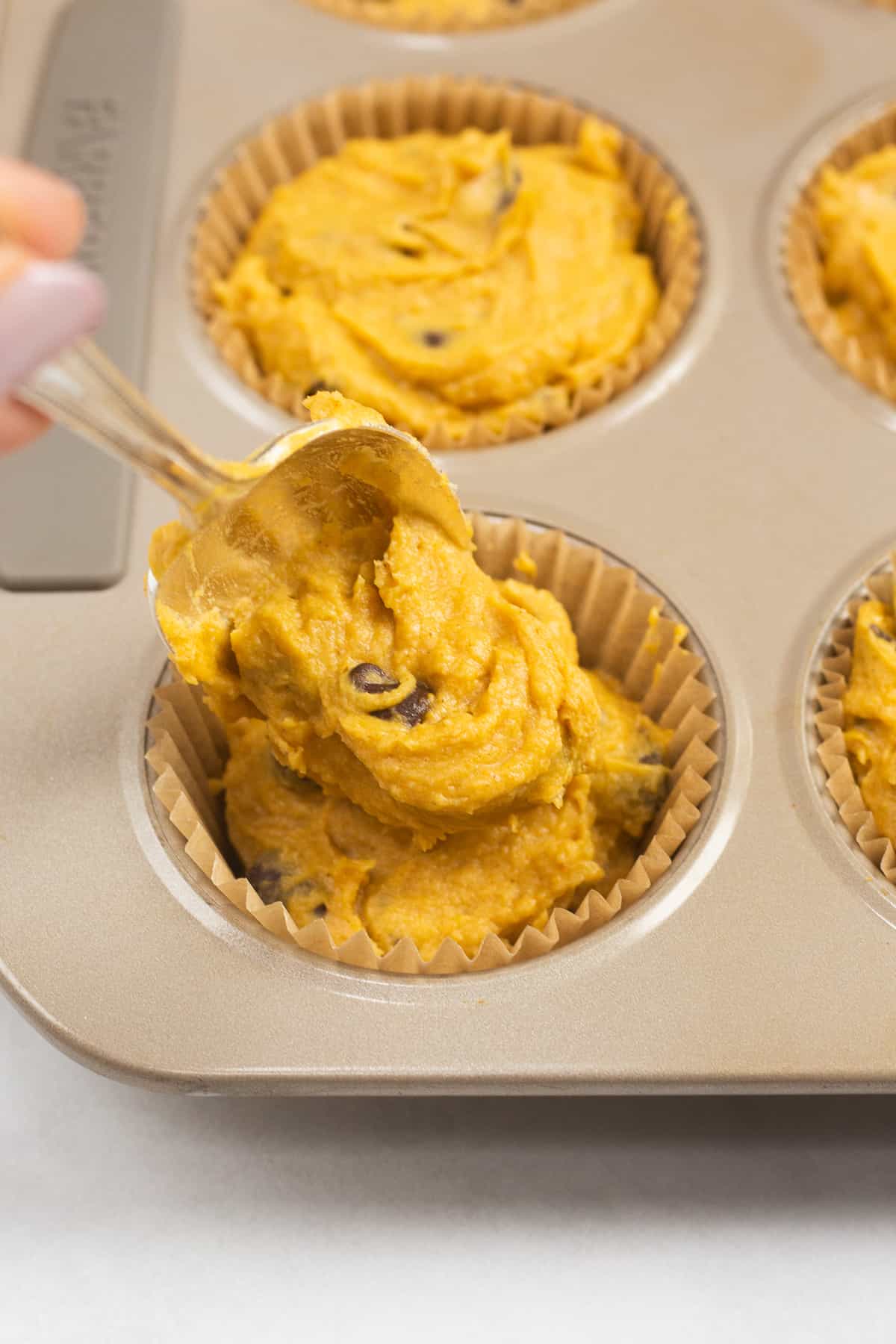 Adding a pumpkin muffin mixture into a muffin tin with a spoon.