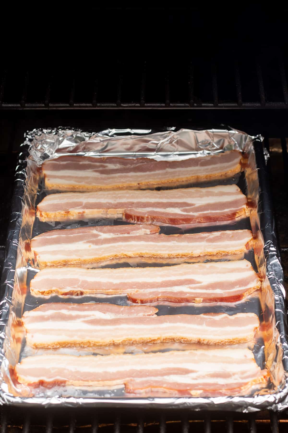 Raw bacon on a foil lined sheet pan on a Traeger grill.