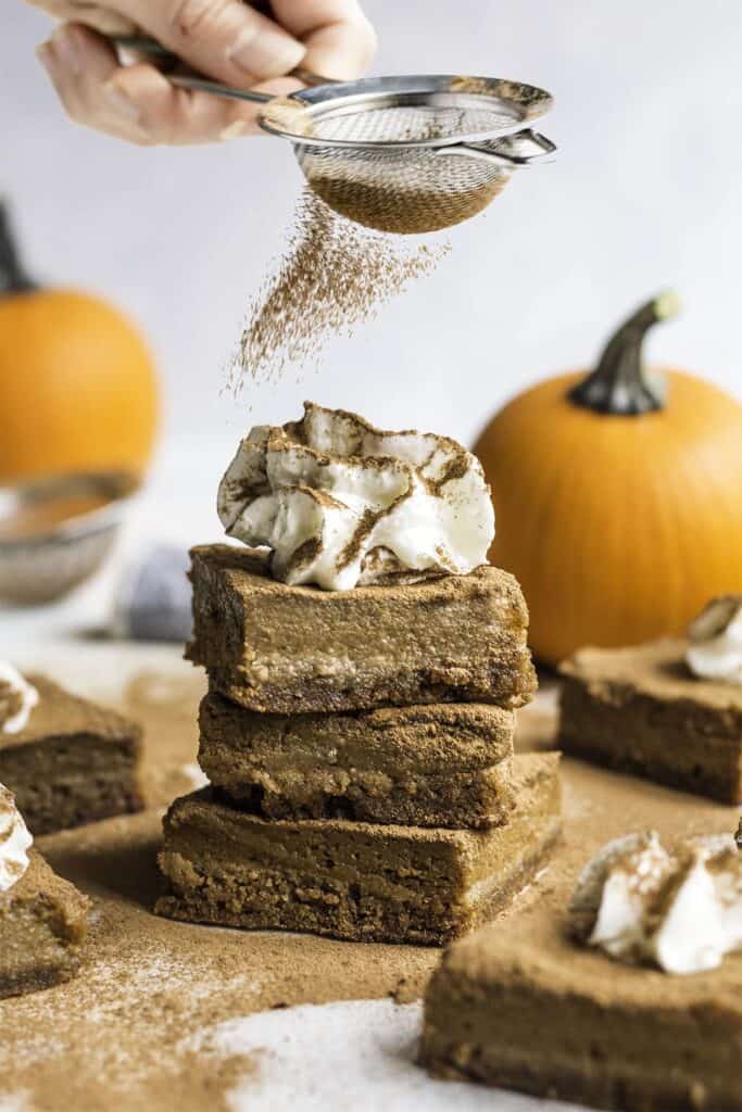 a stack of three pumpkin bars being dusted with cinnamon.