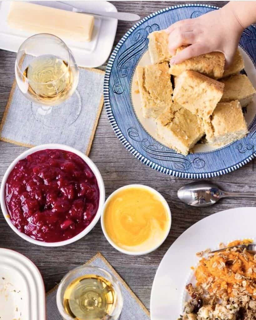A top down shot of a table with holiday sides and a hand reaching for a plate of cornbread.