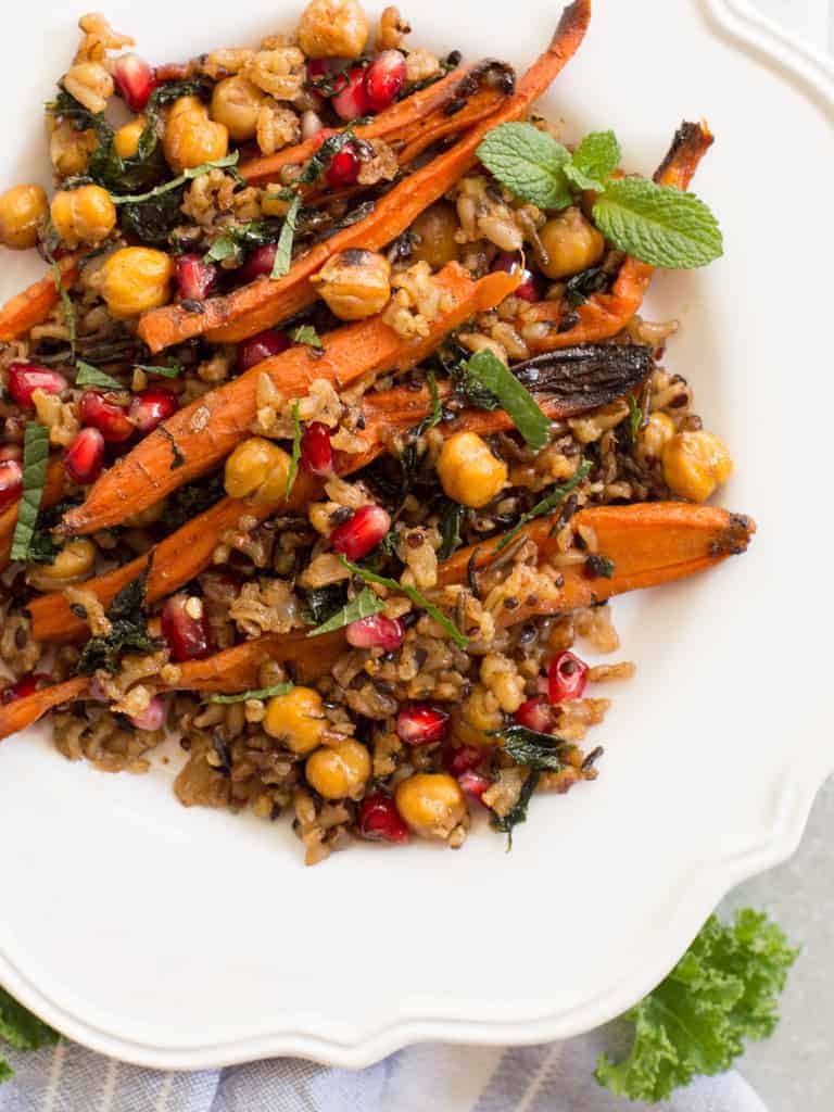 A roasted carrot and chickpea warm salad on a white place with mint garnish.