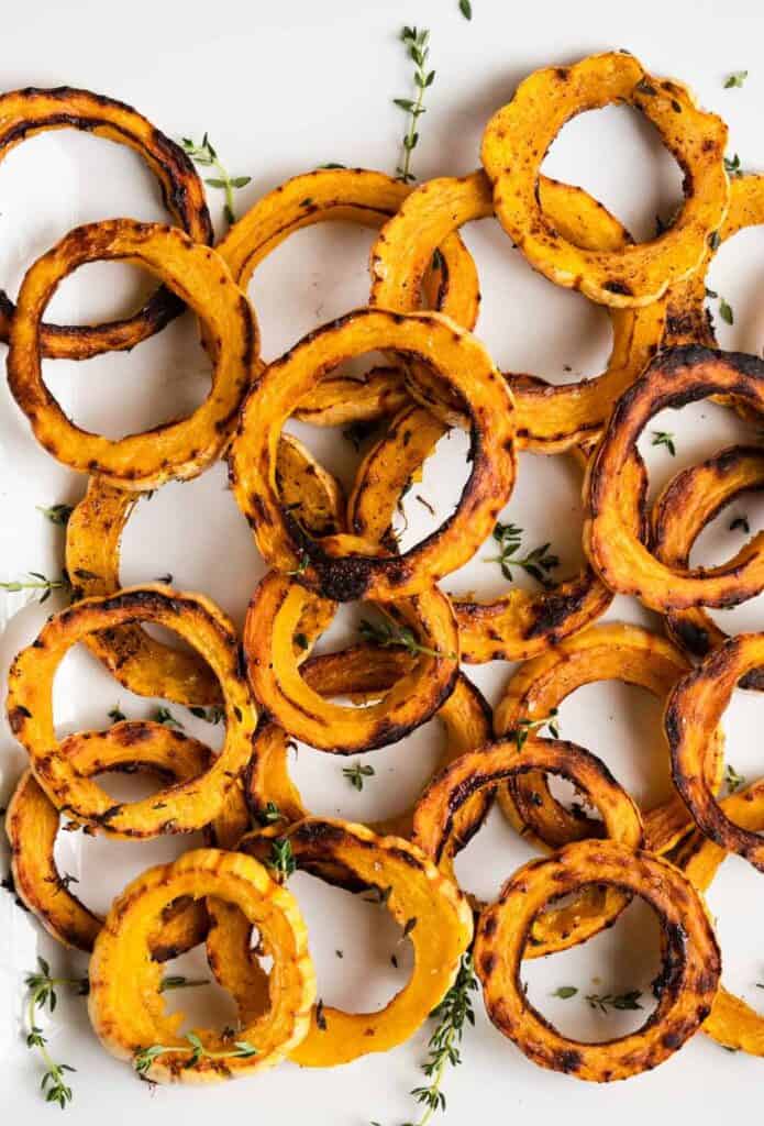 A top down shot of slices of roasted delicata squash on a white background.