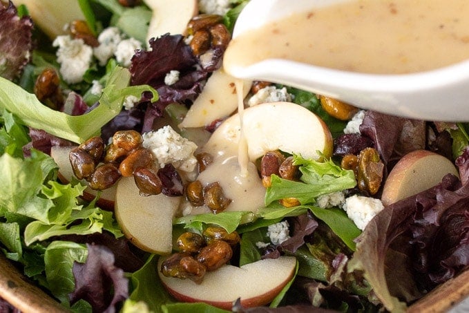 A close up of dressing being poured on an apple pecan salad.