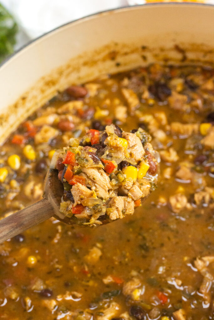 A close up of a wooden spoon lifting some turkey chili out of a large pot.