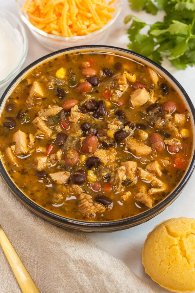 A bowl of turkey chili on a white background surrounded by toppings.