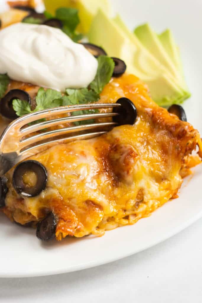 A fork cutting into an enchilada on a white plate.