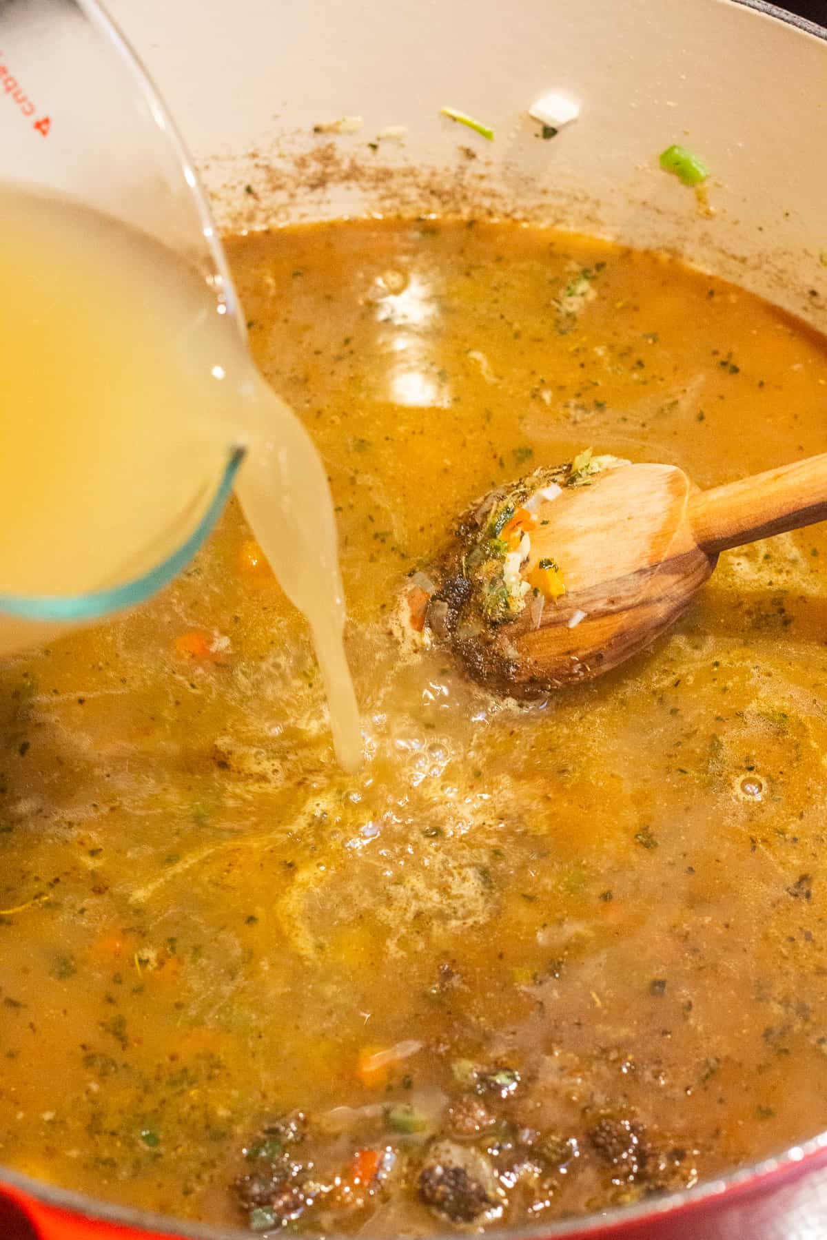 Chicken broth being poured into a large pot with cooked vegetables and spices already in it.