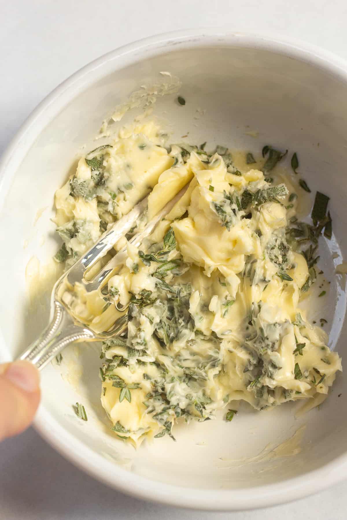 a fork mashing together herbed butter in a white bowl.