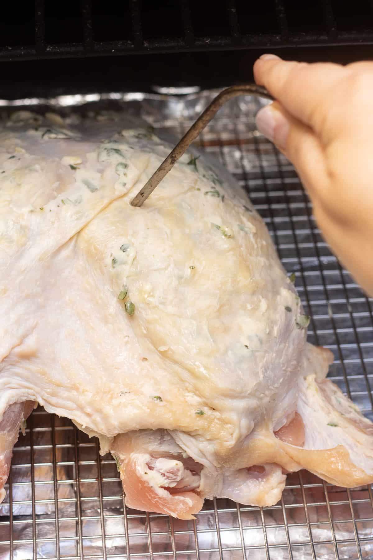a hand pushing a temperature probe into a raw turkey breast on a Traeger grill.