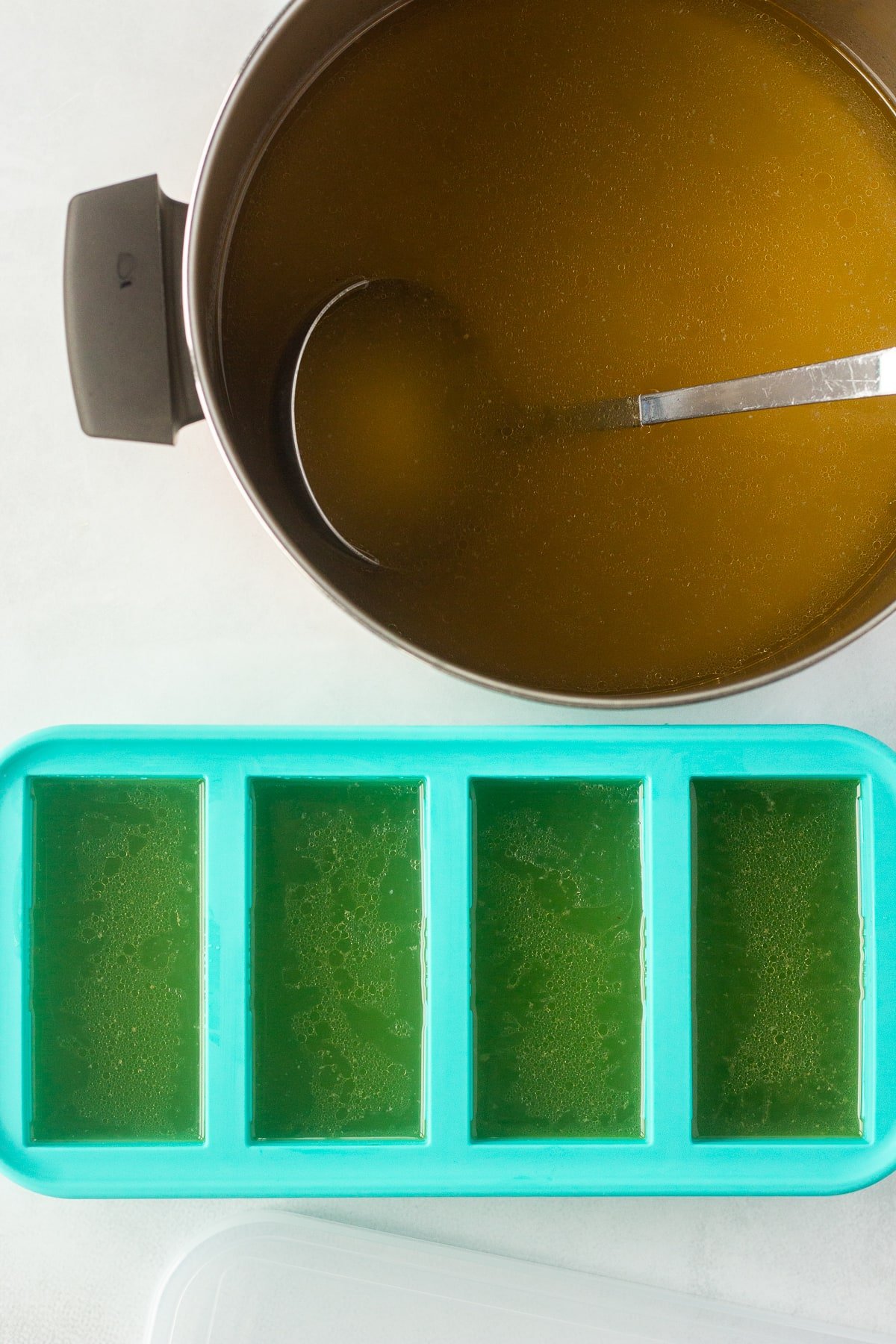 A top down shot of a pot with chicken broth in it next to blue silicone freezer molds to store the broth.