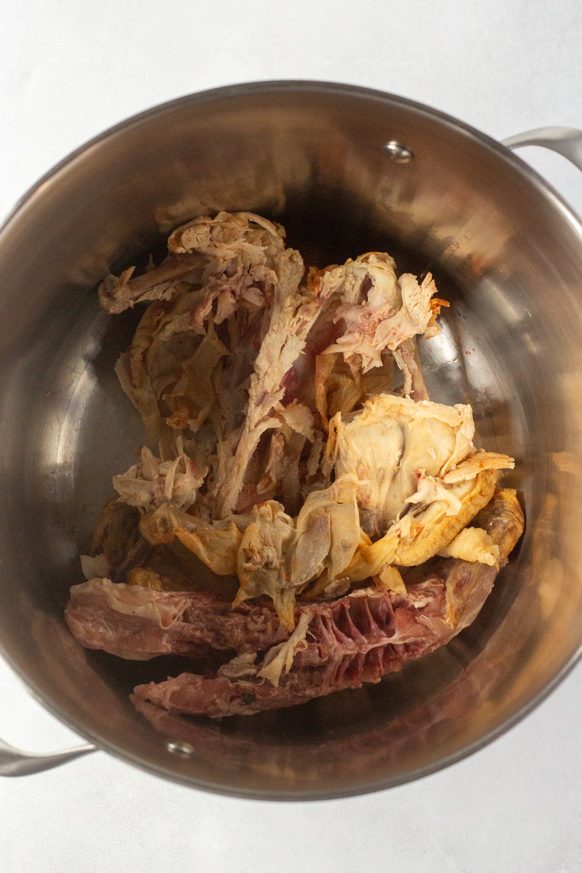 A top down shot of a cooked chicken carcass in a large stock pot.