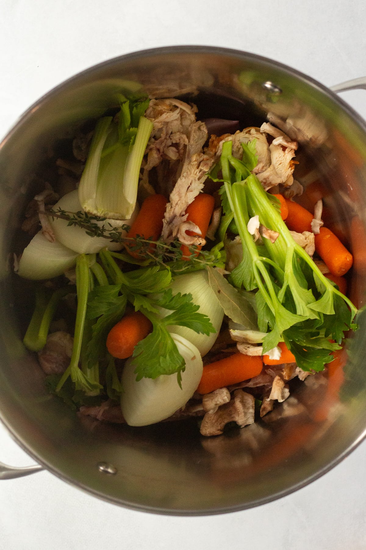 A top down shot of a chicken carcass and cut up veggies in a large stock pot.