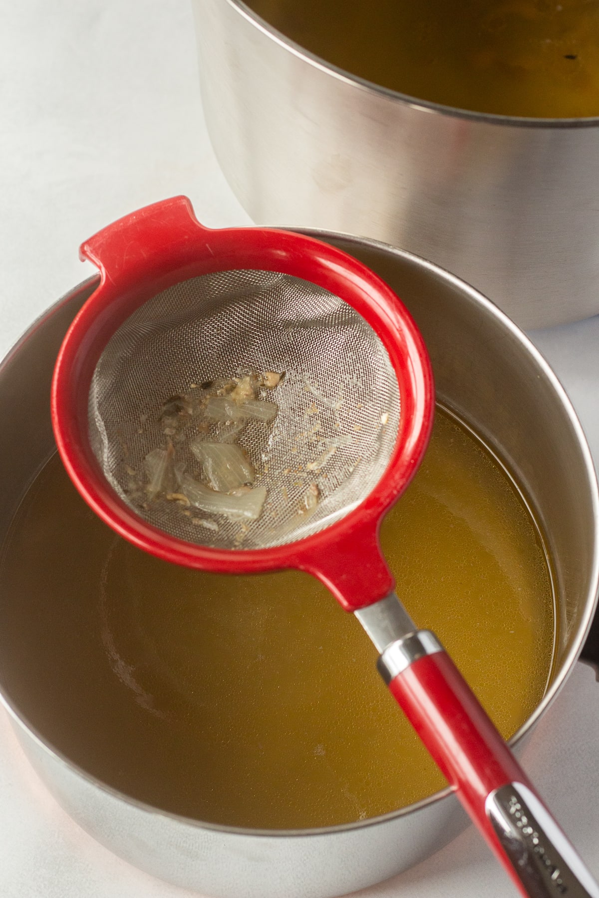 A fine mash strainer over a pot with chicken broth in it.