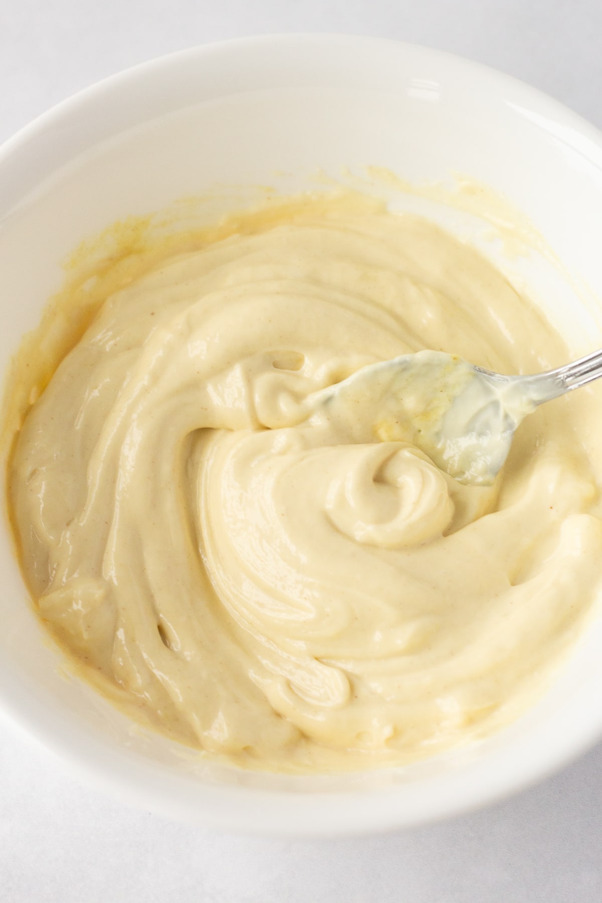 A white bowl with a mixture of mayo and dijon mustard, with a spoon.