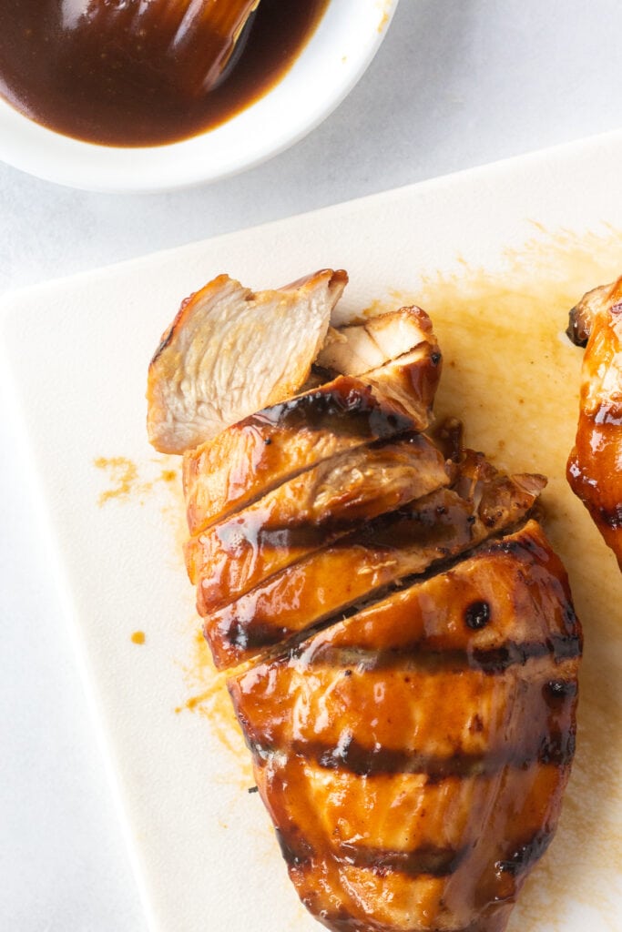 A top down shot of grilled and partially sliced chicken breast on a white cutting board.