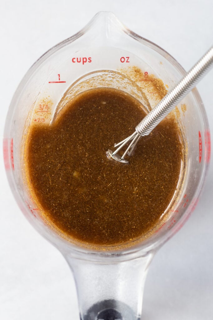 A brown chicken marinade in a measuring cup with a small whisk sticking out.