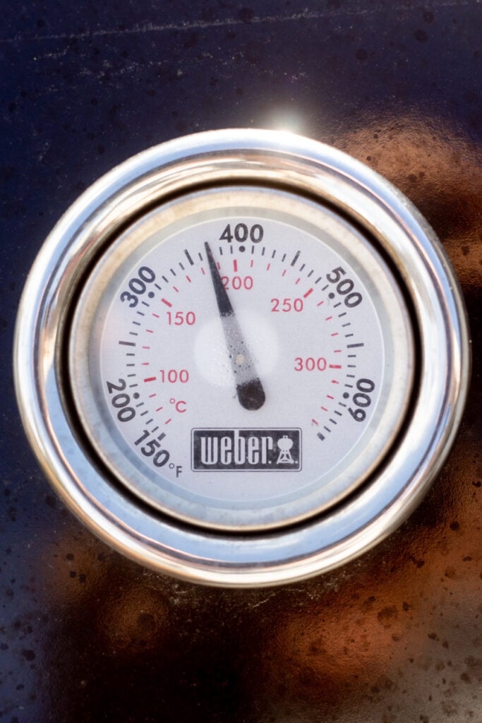Close up of a hood thermometer on a Weber gas grill reading roughly 370F.