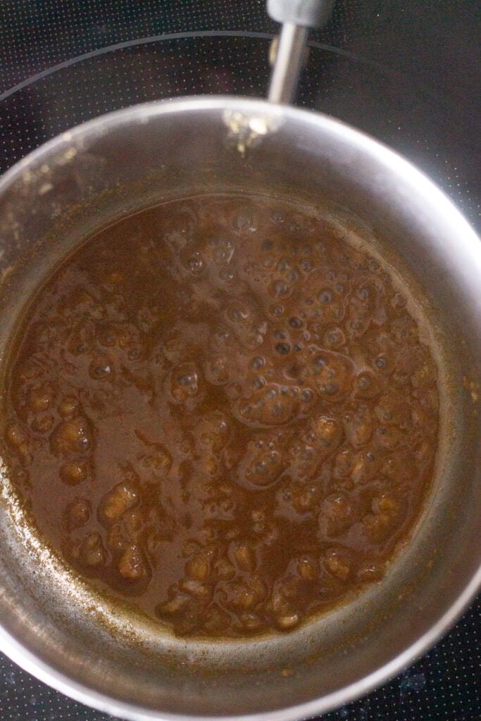 A brown chicken marinade being boiled in a small saucepan on a stovetop.