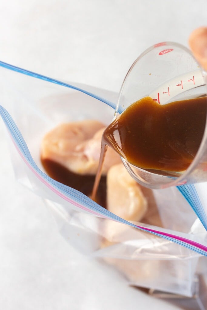Pouring marinade into a ziploc bag with boneless skinless chicken breasts in it.