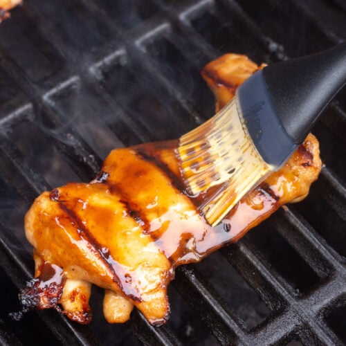 A boneless skinless chicken thigh on the grill being brushed with sauce.