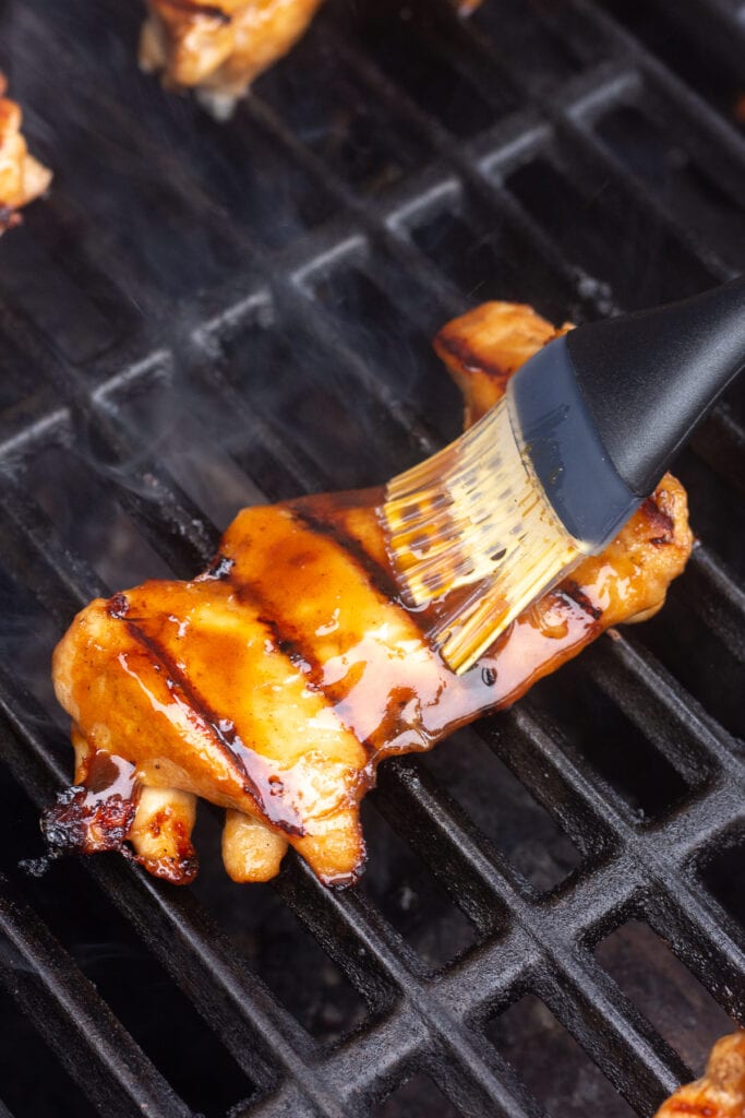 A boneless skinless chicken thigh on the grill being brushed with sauce.