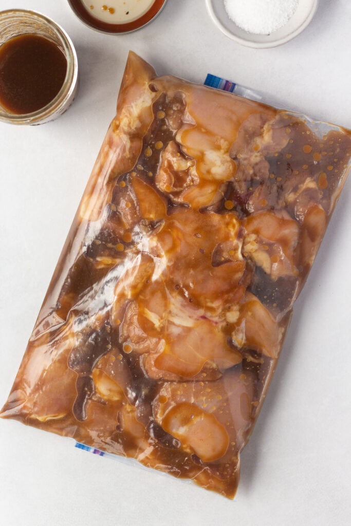 A top down shot of raw skinless boneless chicken thighs marinating in a large ziploc bag.