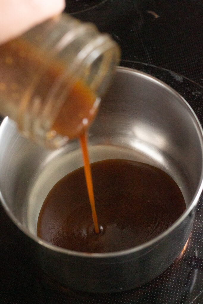 pouring a brown marinade into a small saucepan on the stove.