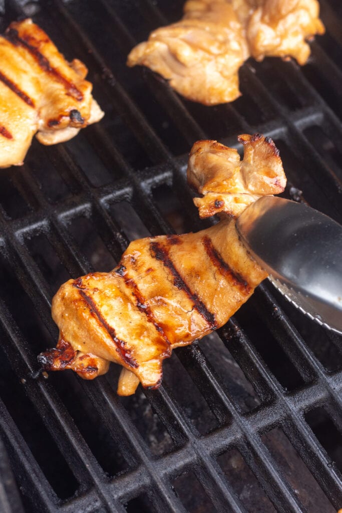 a pair of tongs flipping over a boneless skinless chicken breast on a gas grill.
